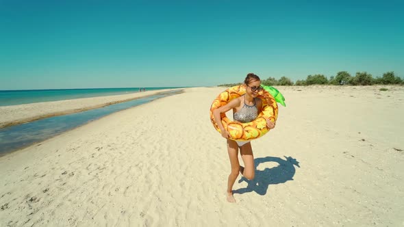 Cheerful Beautiful Young Millennial Woman Running on Empty Sunny Sandy Beach Holding Yellow