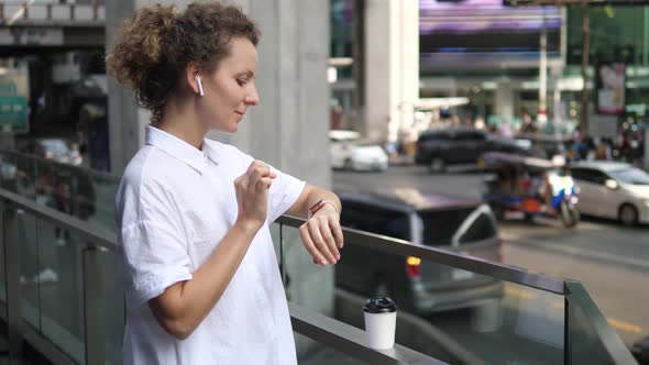 Young Woman Wearing Smartwatch Listening Music In Airpods In City