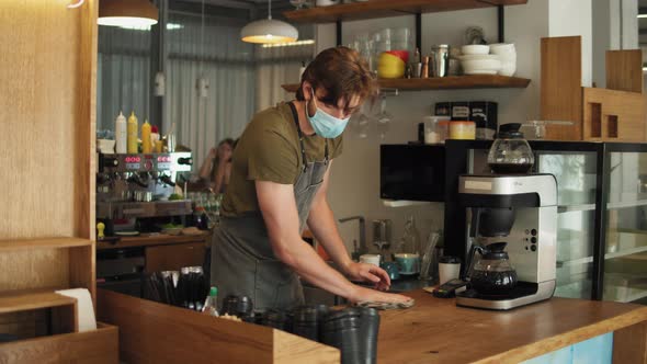 Young Barista Man in Mask and Apron Cleaning and Preparing Bar for Visitors Working in Coffee Shop