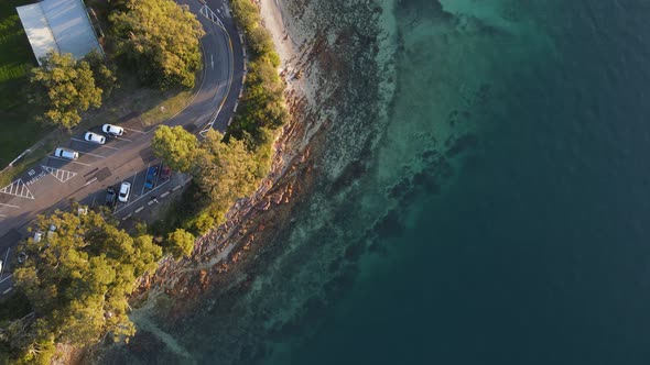 High drone view looking down on a scenic popular swimming area next to a coastal road and car park a