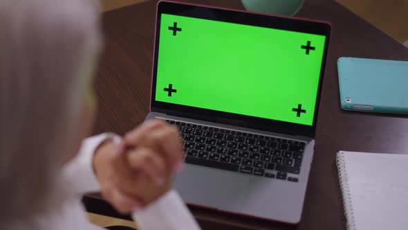 Closeup Chromakey Laptop on Table in Office with Blurred Mature Businesswoman Sitting Indoors