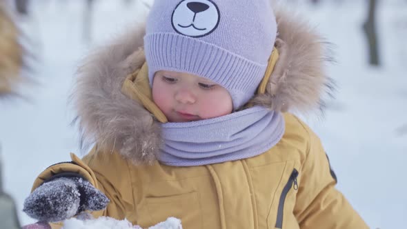 Toddler plays with snow in mother's palm in wintertime, close-up