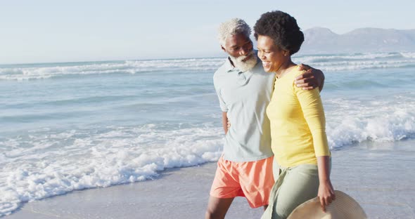 Happy african american couple walking and talking on sunny beach