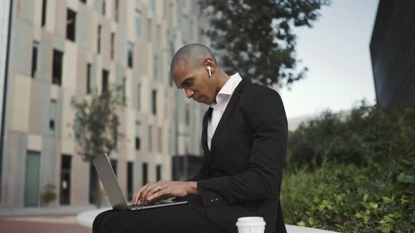 Pensive African businessman working on laptop in headphones