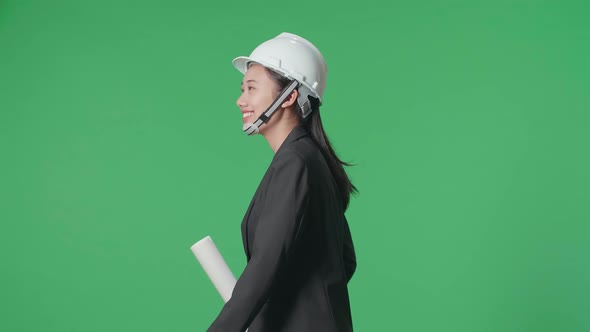 Side View Of Asian Female Engineer With Blueprint Looking Around And Walking On Green Screen