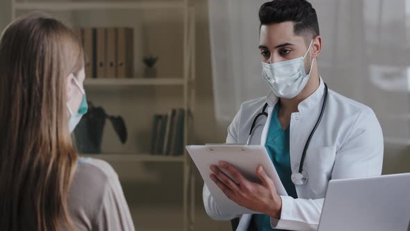 Arabian Male Doctor Physician in Medical Face Mask Making Notes on Clipboard Consulting Female