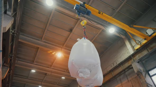 overhead crane with metal iron chains and mighty hooks carries big white bags. A workshop crane