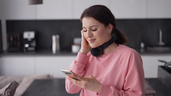 Pretty Young Woman in Headphones Dancing in Kitchen and Listening Music