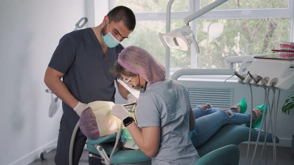 Female Dentist with Help an Male Assistant and Medical Equipment Works with Patient in Dental Office