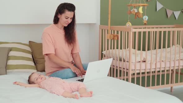 Busy Mom Works Using Laptop While Baby Sleeps Next to Her