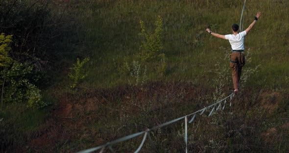 A Man in White Shirt Is Balancing on the Slackline Over the Quarry Extreme