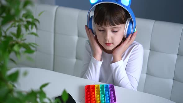 Baby Girl Playing with Rainbow Pop It Fidget and Listening Music with Headphones
