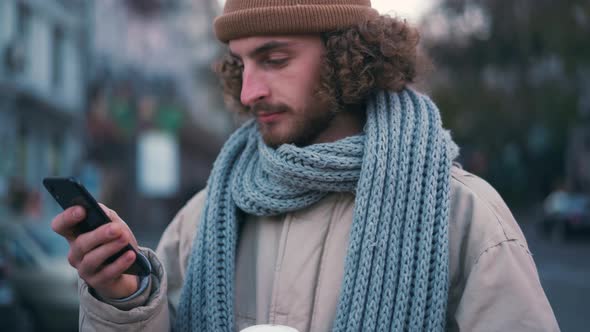 Happy curly-haired man texting by phone