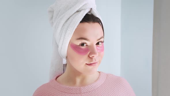 A woman in front of a mirror applies hydrogel collagen pink patches under her eyes.
