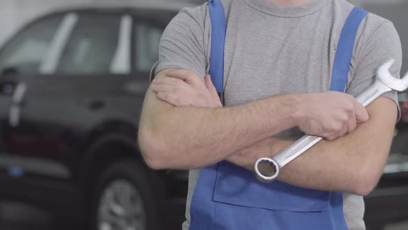 Unrecognizable Caucasian Man in Blue Workrobe Crossing Hands with Wrench at the Background of Black