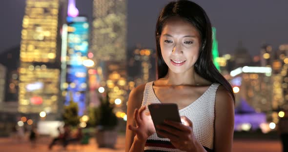 Woman looking at mobile phone in the city at night 