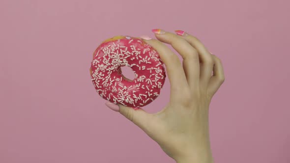 Womens Hand Holding Red, Delicious, Sprinkled Donut on Pink Background.