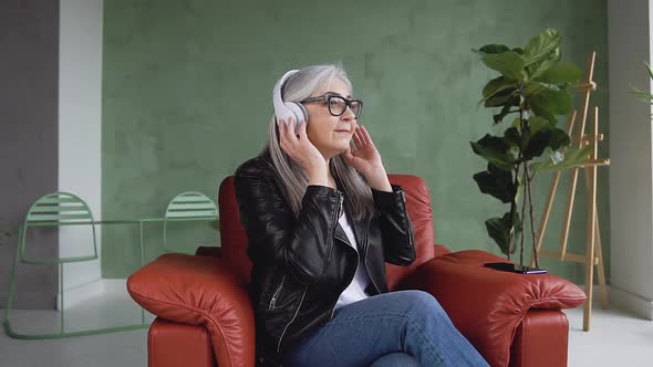 Older Woman in Stylish Jacket which Enjoying the Beautiful Music on Headphones