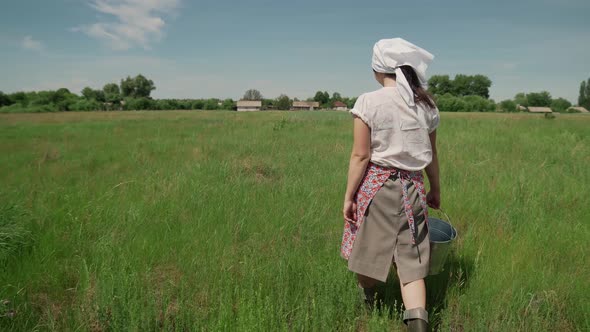 Young Milkmaid in Sunny Summer Carries a Bucket and Walks on the Grass