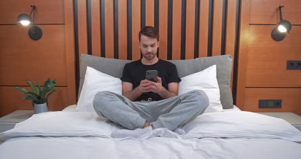 Young Man Sits on the Bed and Playing Game on a Smartphone Man Wins the Game Emotions of Victory