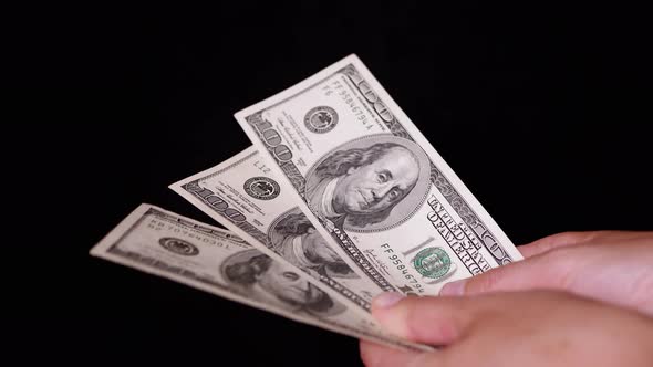 Hand Holding Three 100 Dollar Bills on Isolated Black Background