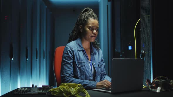 African american female computer technician using laptop working in business server room