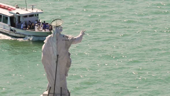 Tourist ferry going across river passing statue of a saint, sightseeing tour