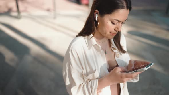 Pleased brunette woman in headphones texting on phone