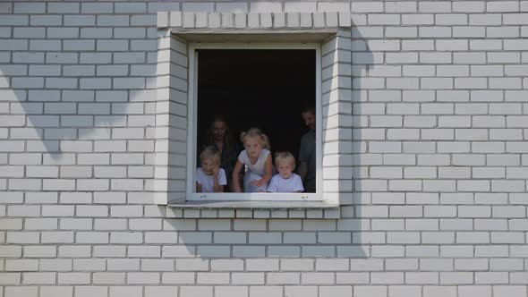 A Friendly Family Appears in the Window of Their House. alt