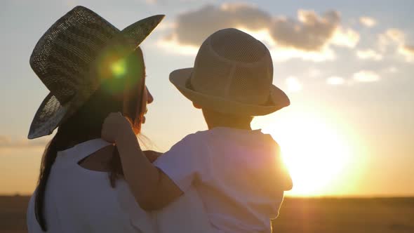 Mother and Little Son Playing on Meadow. Boy Raising Up Hands at Wonderful Sunset Through the