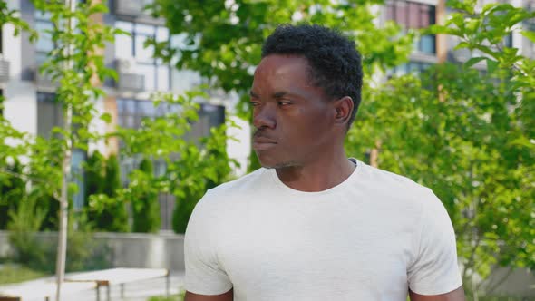 Close Up African Man Looking Away on Background Building and Trees in Summer