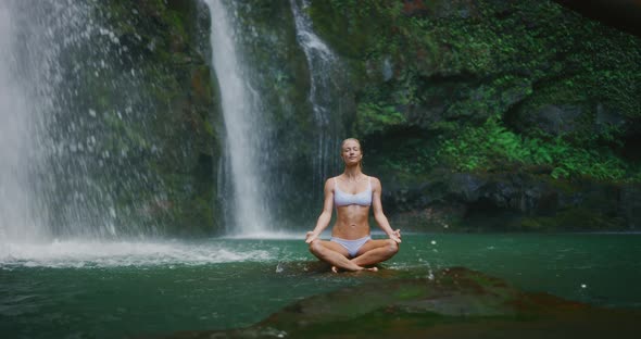 Woman meditating in front of waterfall