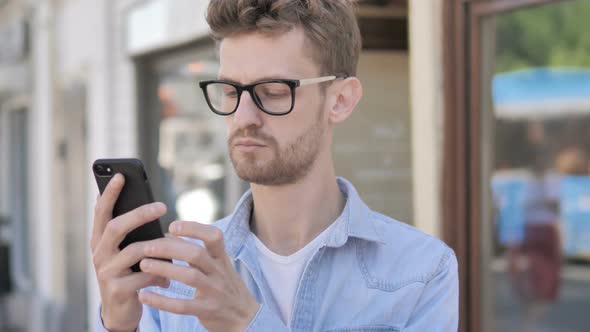 Casual Young Man Using Smartphone while Standing Outdoor