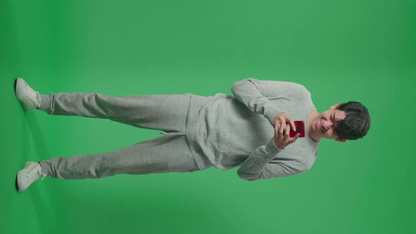 Full Body Of Asian Man Enjoy Using Mobile Phone While Standing On Green Screen In The Studio