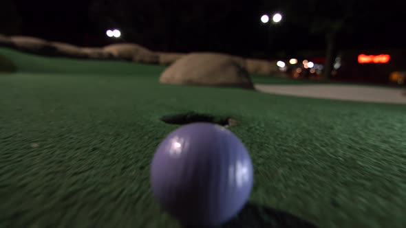 A purple mini golf ball falls into the golf hole and bounces in the pocket on a course.