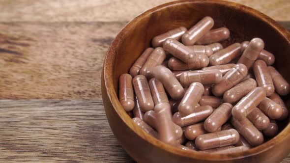 Brown pharmaceutical medical capsules fall into a wooden bowl on a wood rustic vintage table