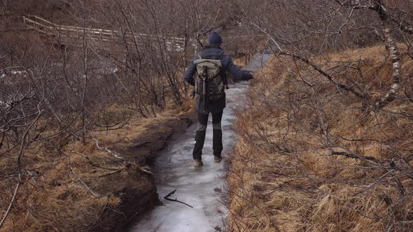 Man Tourist with a Backpack Walking on an Ice Covered Trail Through Dry Forest