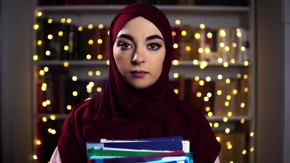 Close Up of Young Muslim Student Standing at a Bookshelf with Garland Background and Holding Folders