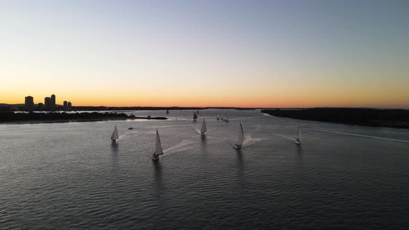 High panoramic drone viewing towards a group of sailing boats racing along the water in the afternoo