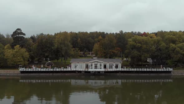 The Camera Flies Over the Water Towards a Beautiful White Restaurant with a Pier Standing Against