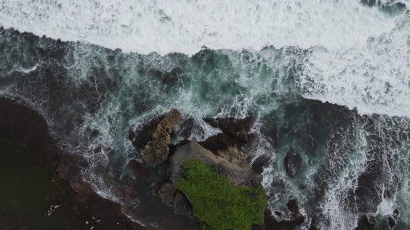 Top down aerial view of giant ocean waves crashing and foaming in coral beach