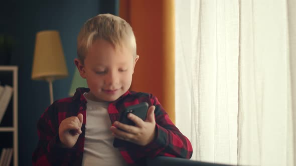 Boy Sitting in Front a Sofa and Making a Video Call Via Smartphone at Home alt