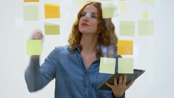 Businesswoman writing on the sticky notes stuck over glass 4k
