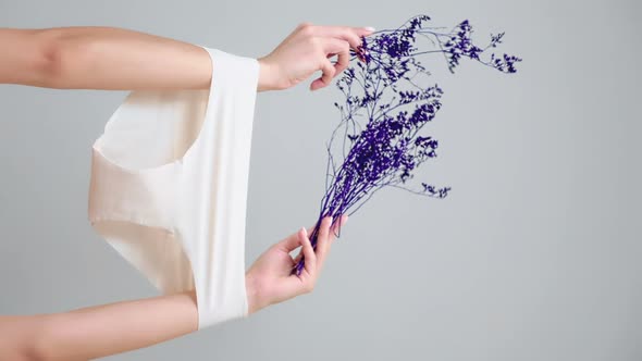 Female's hands, which hold dry violet plants, arms are wearing white panties