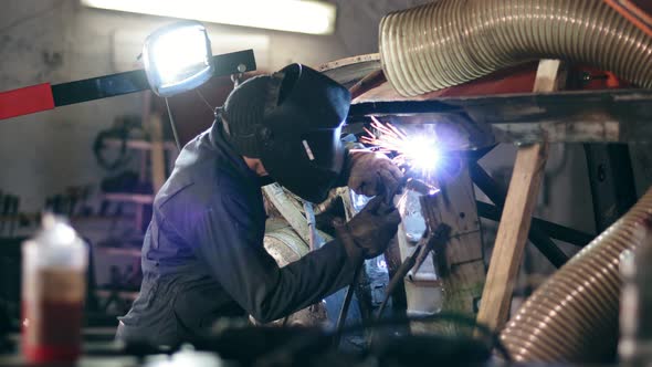 Male Worker at a Welding Factory in a Welding Mask is Working with Metal Construction