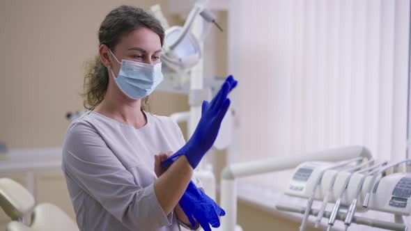 Young Confident Caucasian Female Dentist in Face Mask Putting on Gloves Looking at Camera in Slow