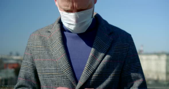 Close-up of Men's Hands with a Smartphone. a Man Has Put a Disposable Mask on His Face and Is