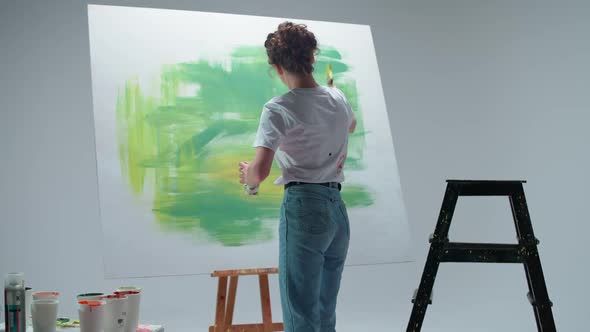 Female Artist Draws with a Brush on a Large Canvas in a White Room a Talented Artist Draws a Color