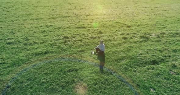 Low Orbital Flight Around Man on Green Grass with Notebook Pad at Yellow Rural Field