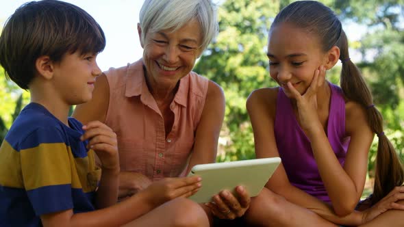 Grandmother and grand kids using digital tablet in the park